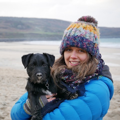 Gemma Ives holding a black puppy on the beach side